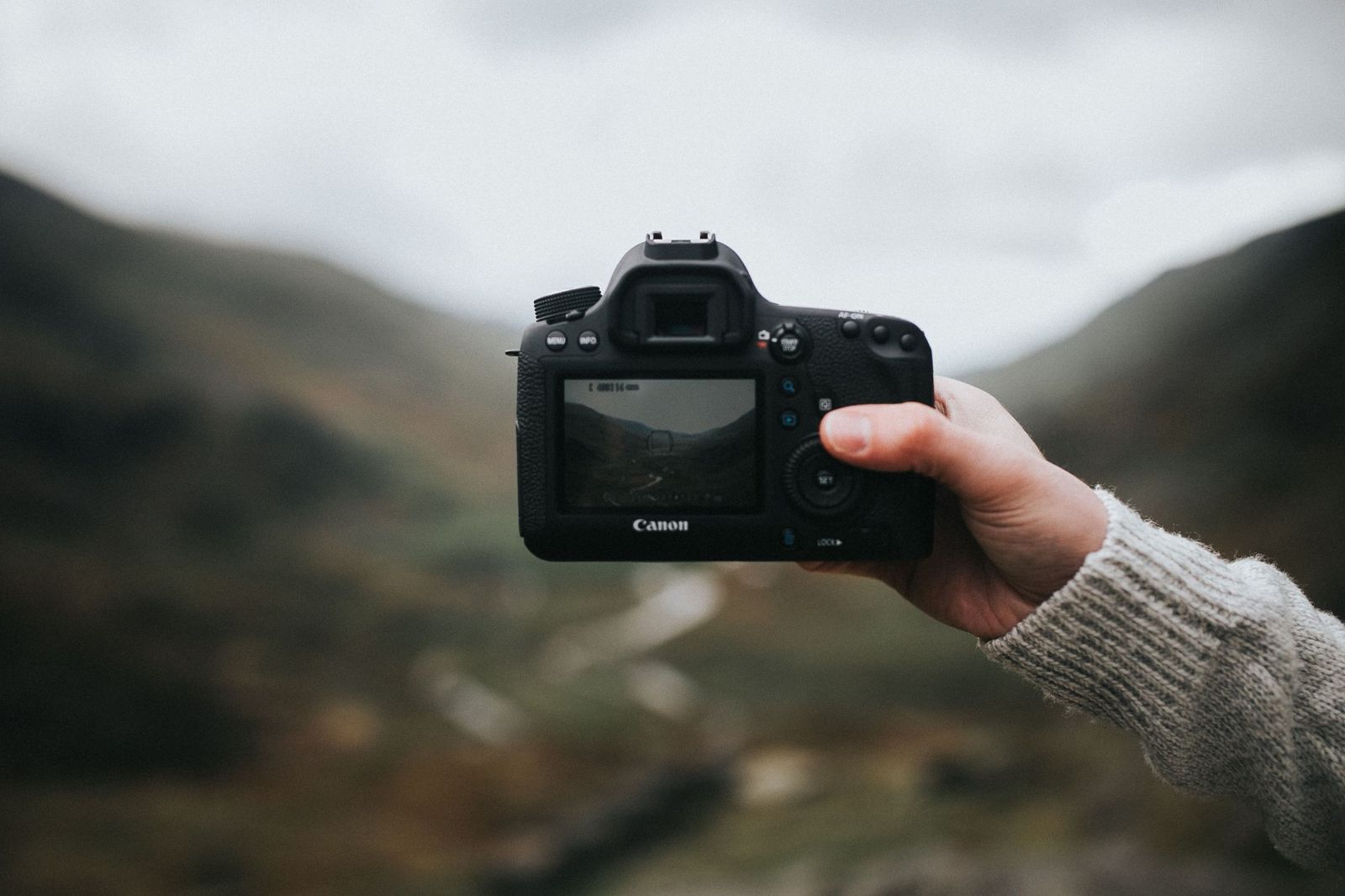 Hand holding a camera up to frame a misty valley on its screen