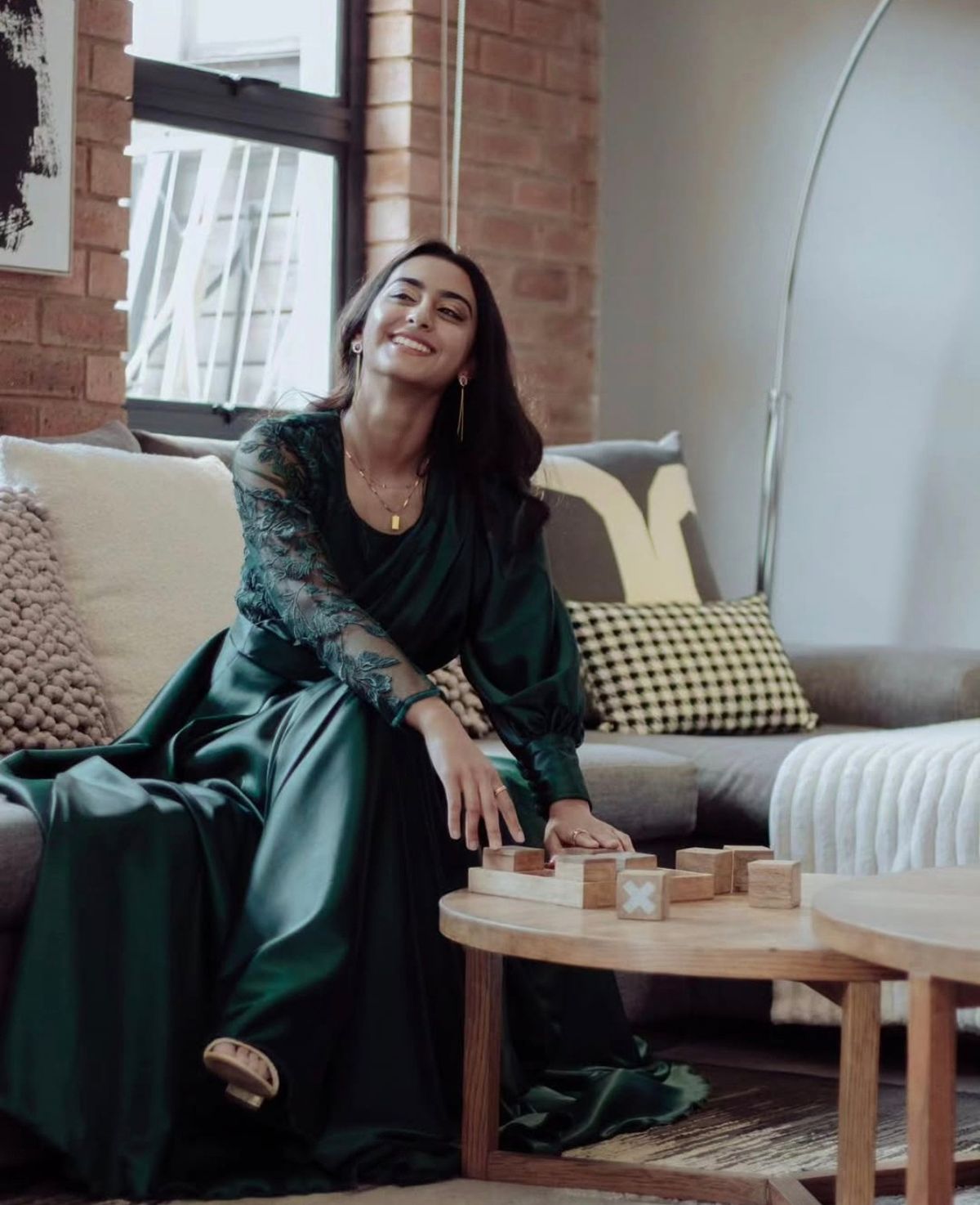 Woman in an emerald gown laughing on a sofa beside a coffee table
