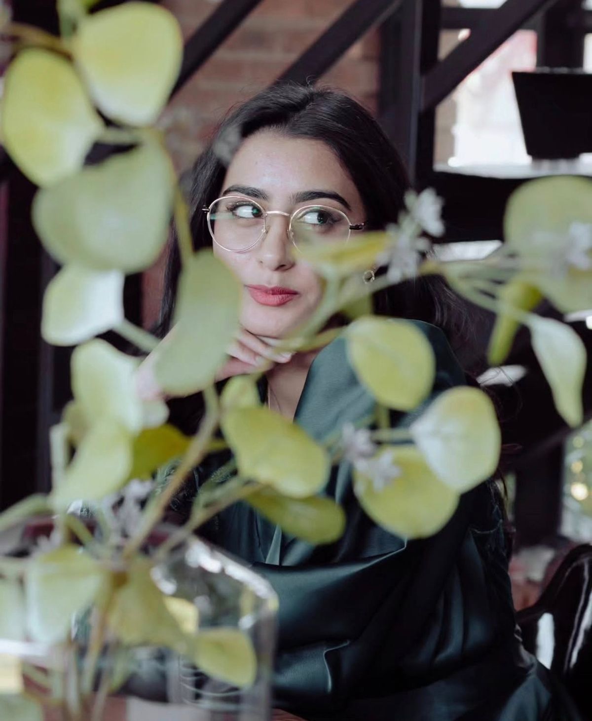 Portrait of a woman in round glasses glimpsed through green leaves