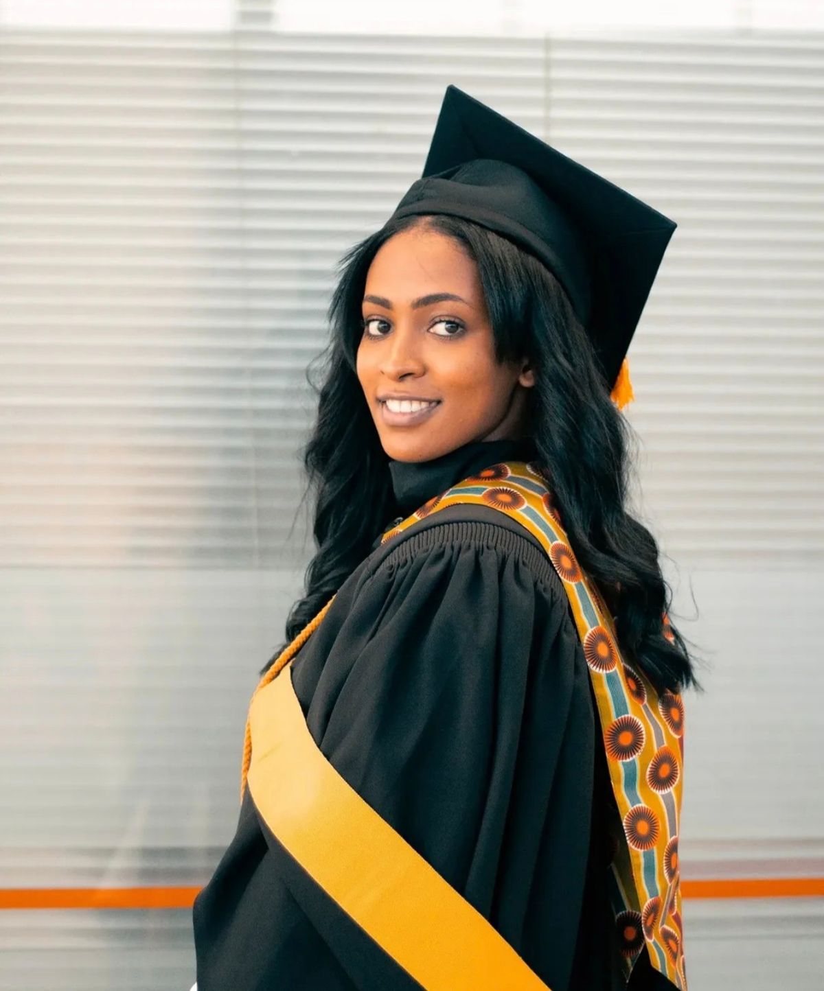 Graduate in cap, gown and patterned stole smiling over her shoulder