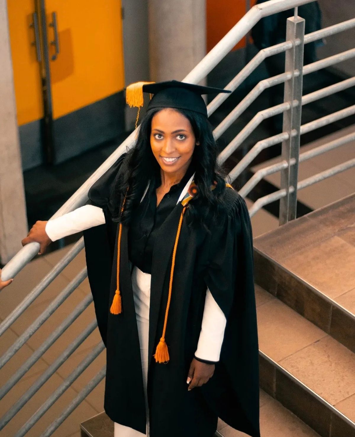 Graduate in cap and gown standing on a staircase