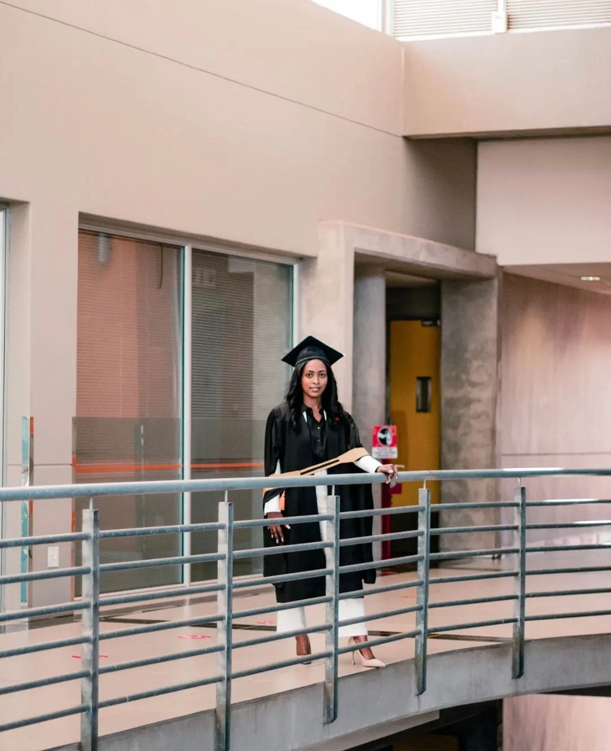 Graduate in cap and gown on a walkway inside a campus building