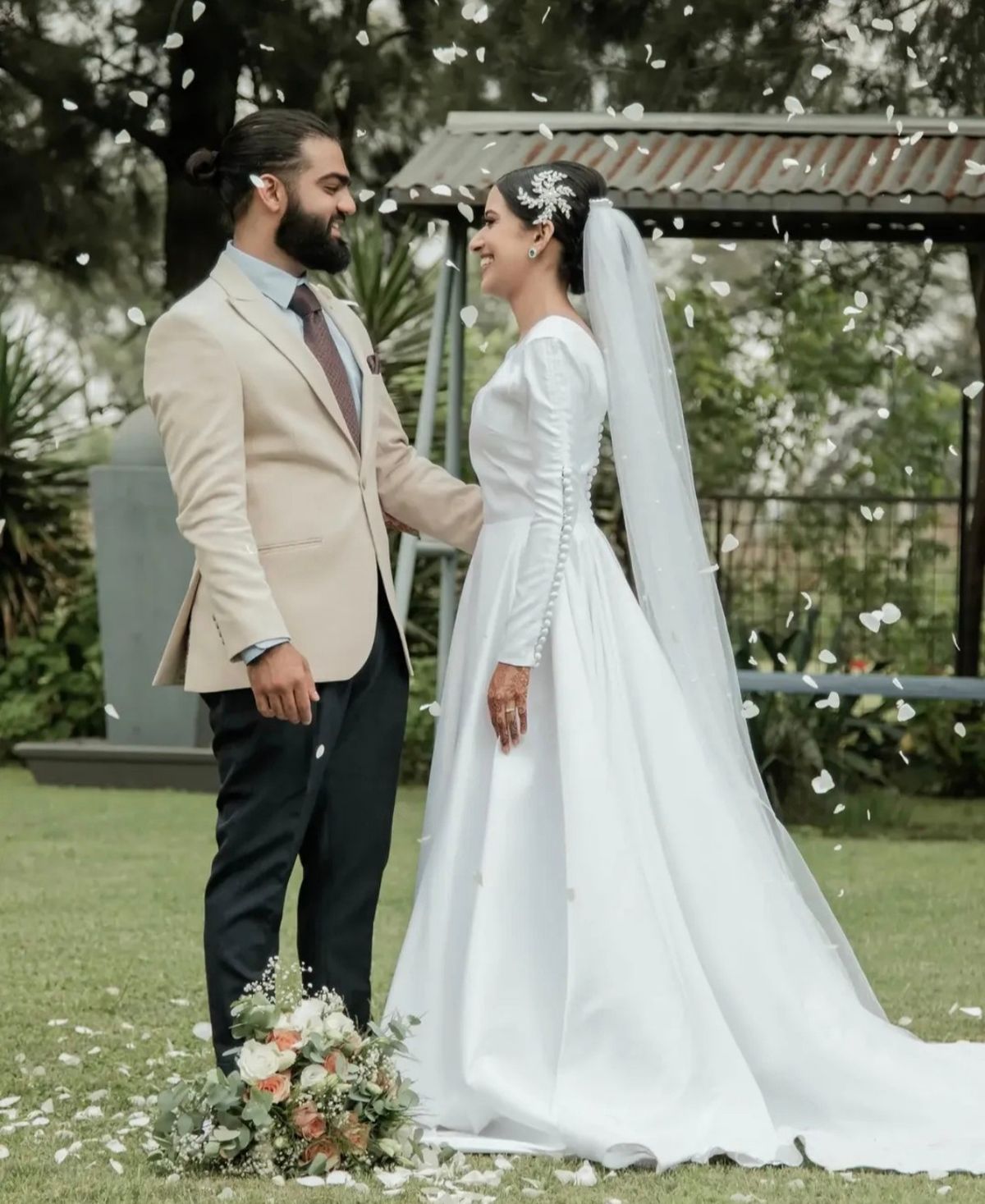 Bride and groom smiling at each other as petals fall around them