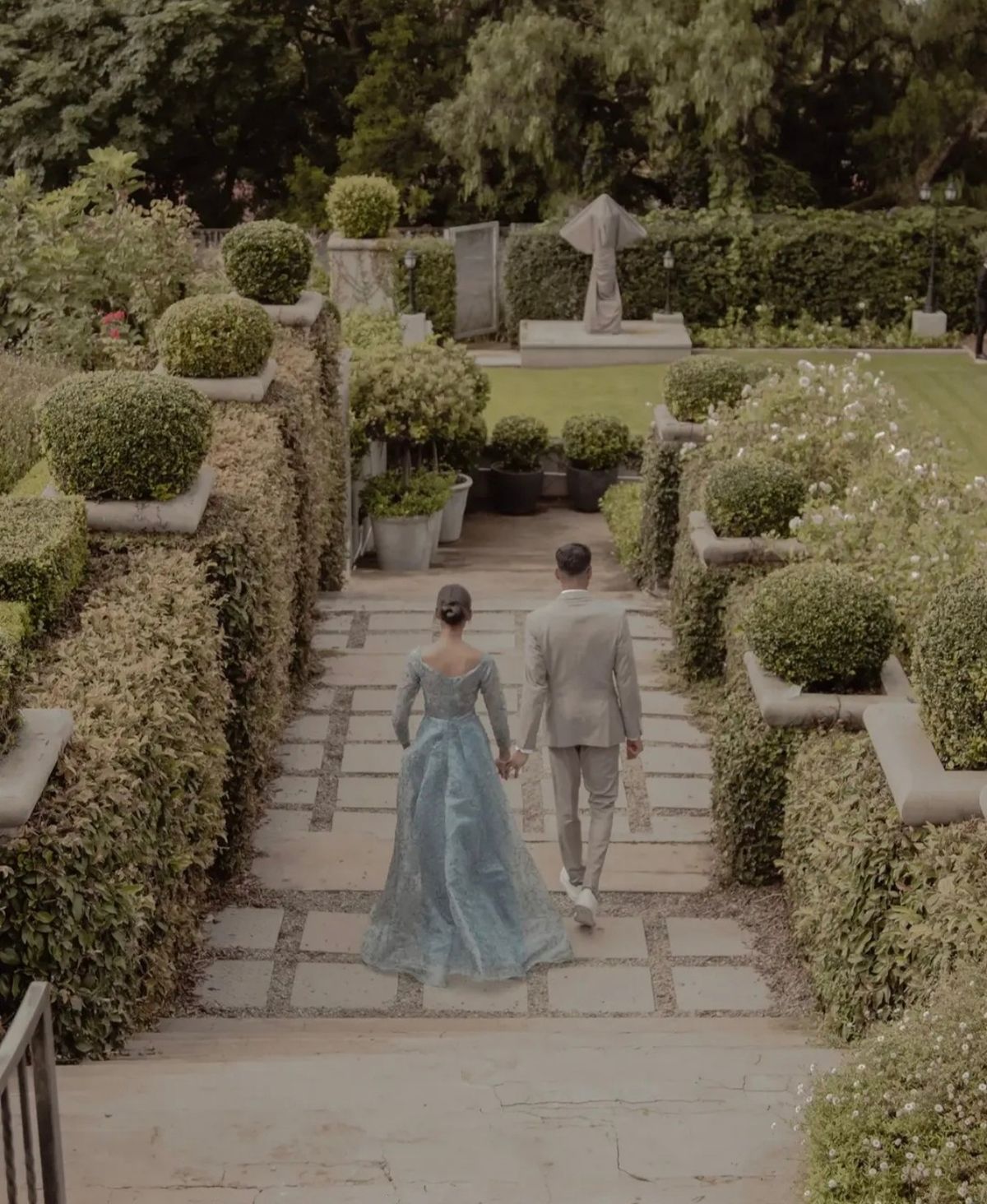 Couple walking hand in hand down a garden path, seen from behind