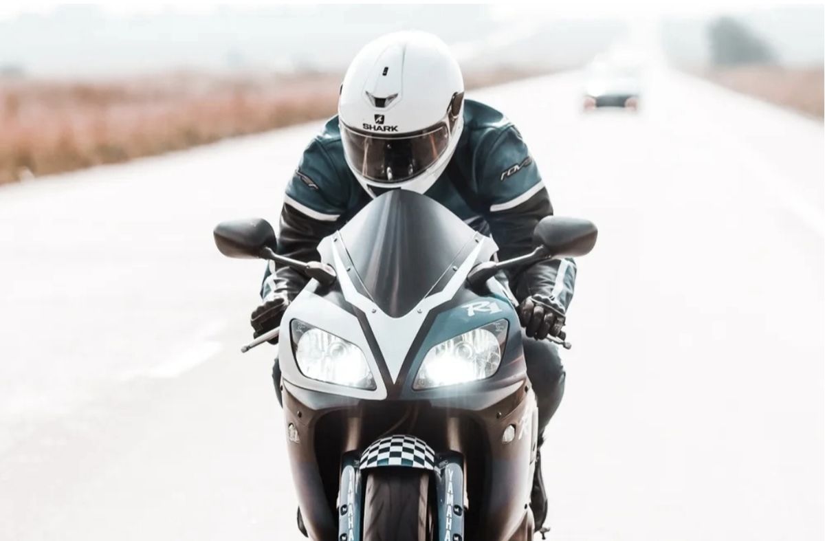 Rider in a white helmet on a sports bike, head-on on an open road
