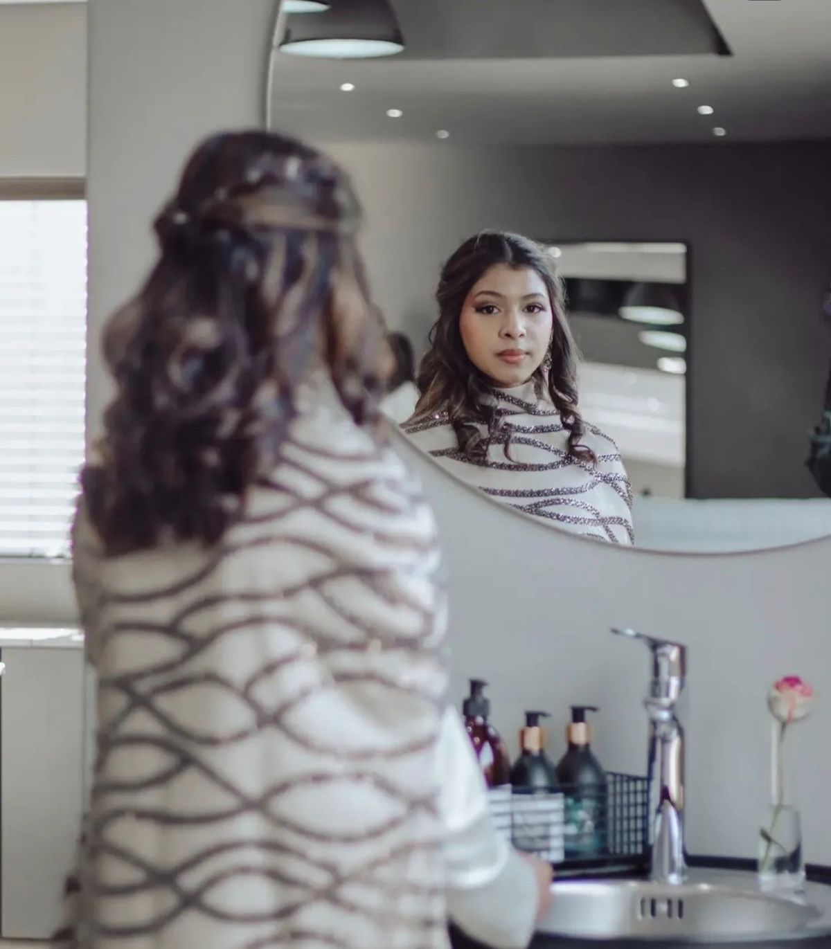 Young woman in a beaded white shawl looking at her reflection in a round mirror