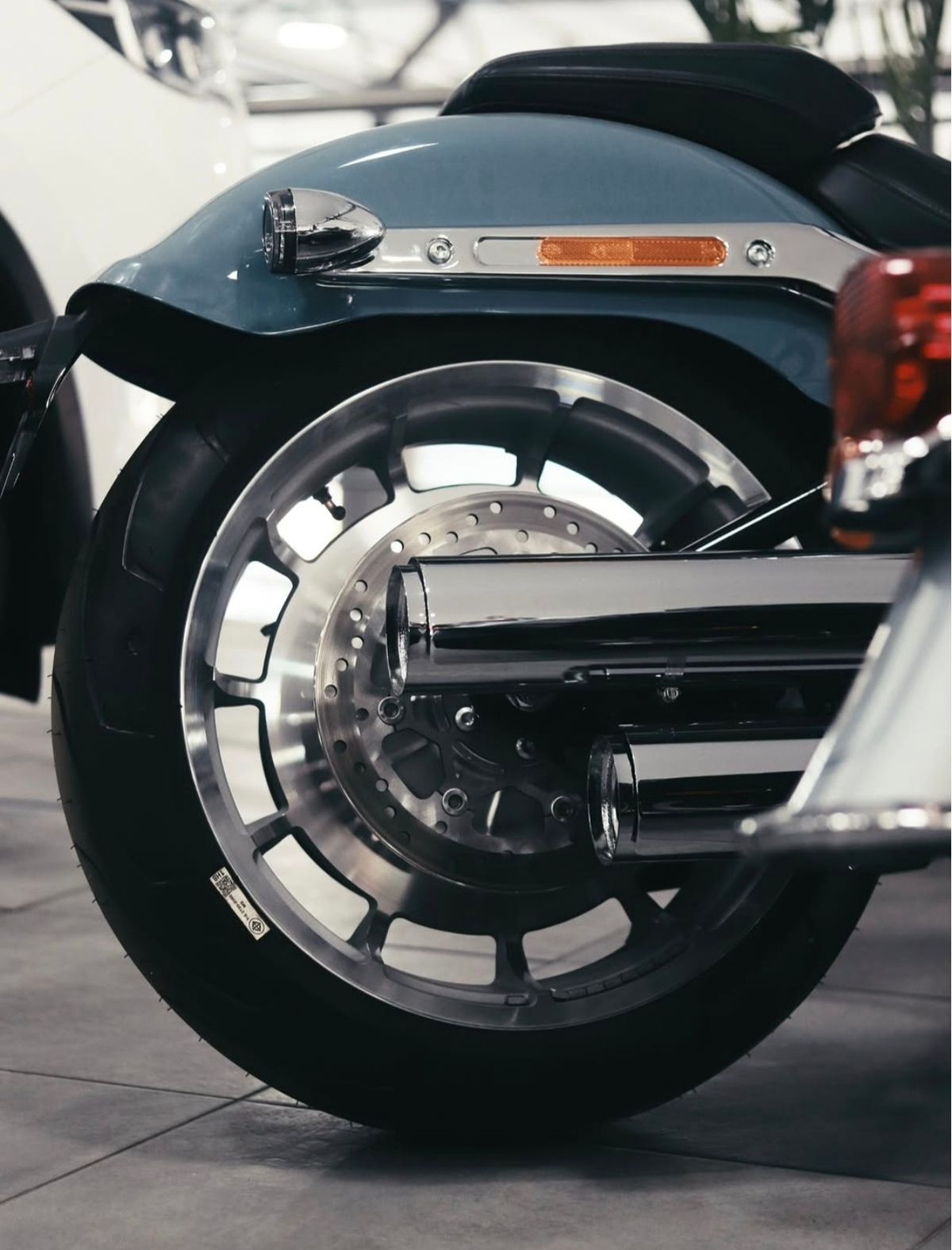 Rear wheel, chrome exhausts and blue fender of a cruiser motorcycle