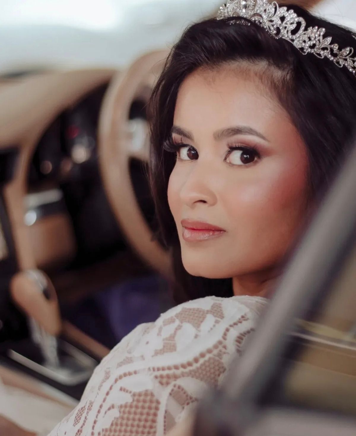 Bride in a tiara and lace dress looking back over her shoulder from a car