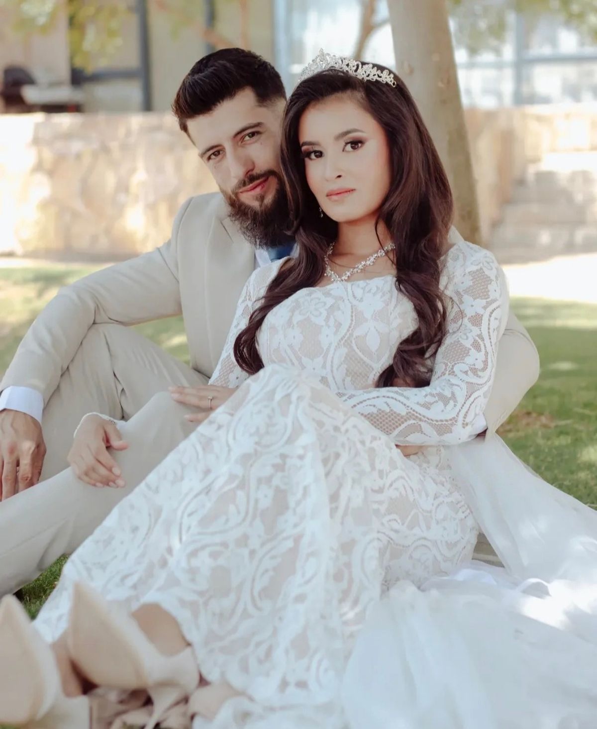 Bride and groom seated together on the grass under a tree