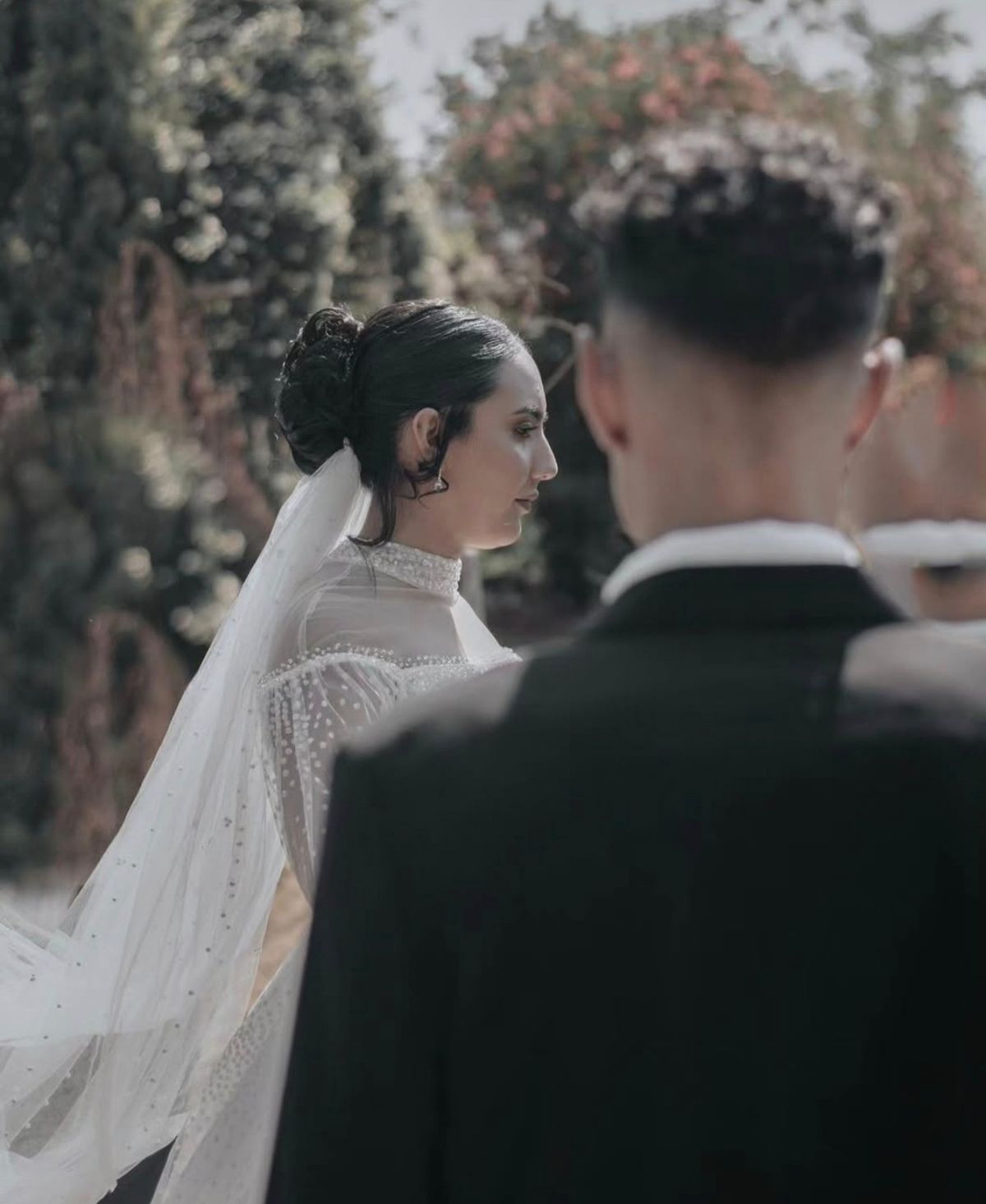 Bride in a beaded veil seen in profile past the groom’s shoulder