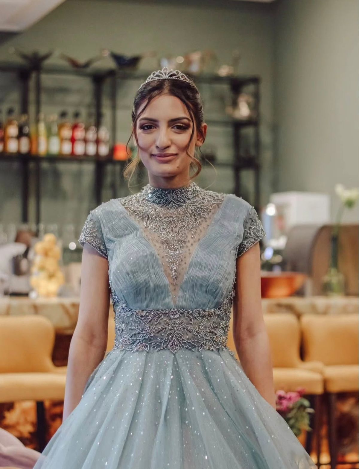 Woman in a beaded pale blue gown and tiara smiling at the camera