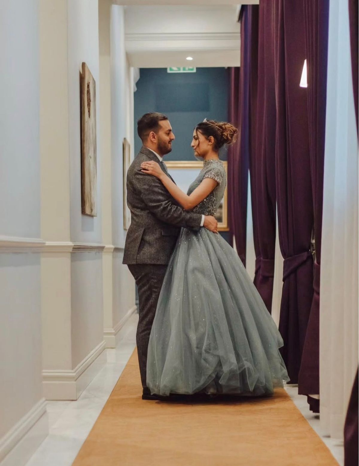 Couple embracing in a hallway, she in a full pale blue gown