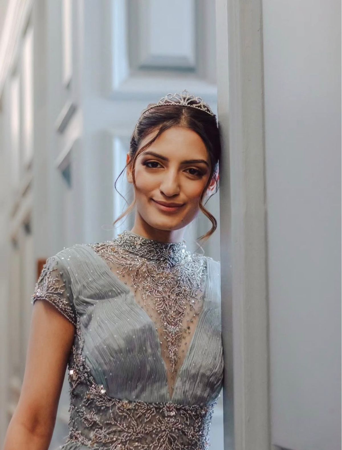 Portrait of a woman in a tiara and beaded gown leaning against a wall