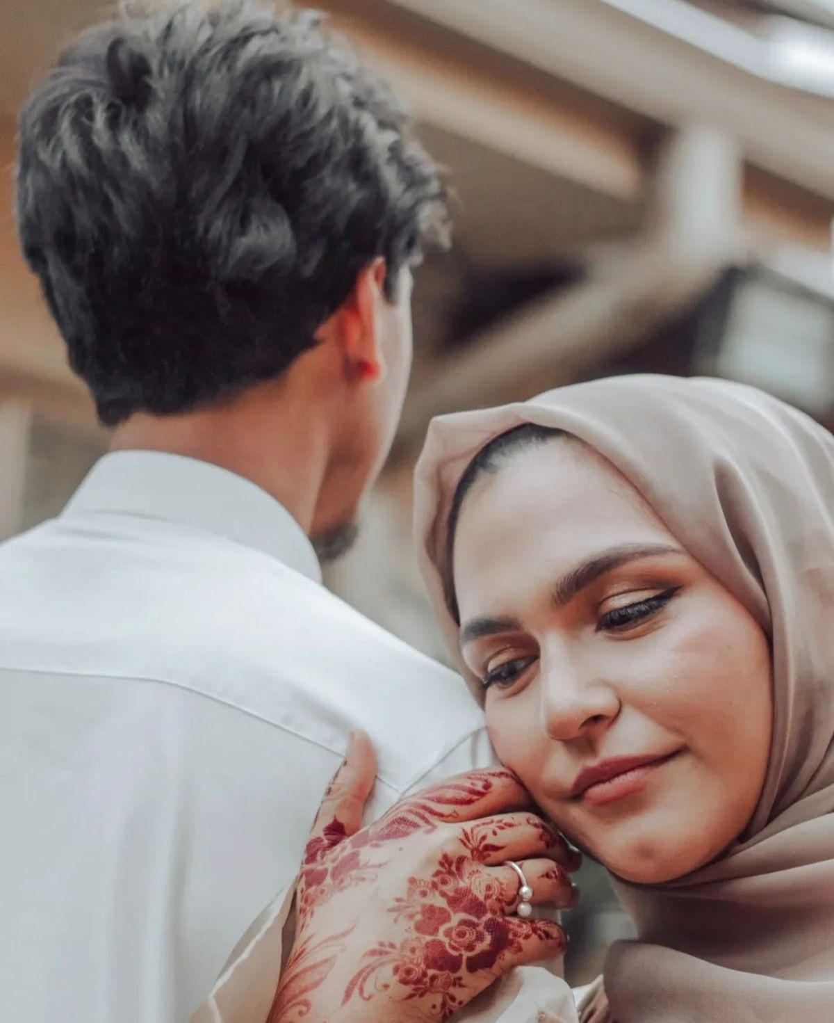 Woman in a headscarf resting her cheek on her hennaed hand at his shoulder